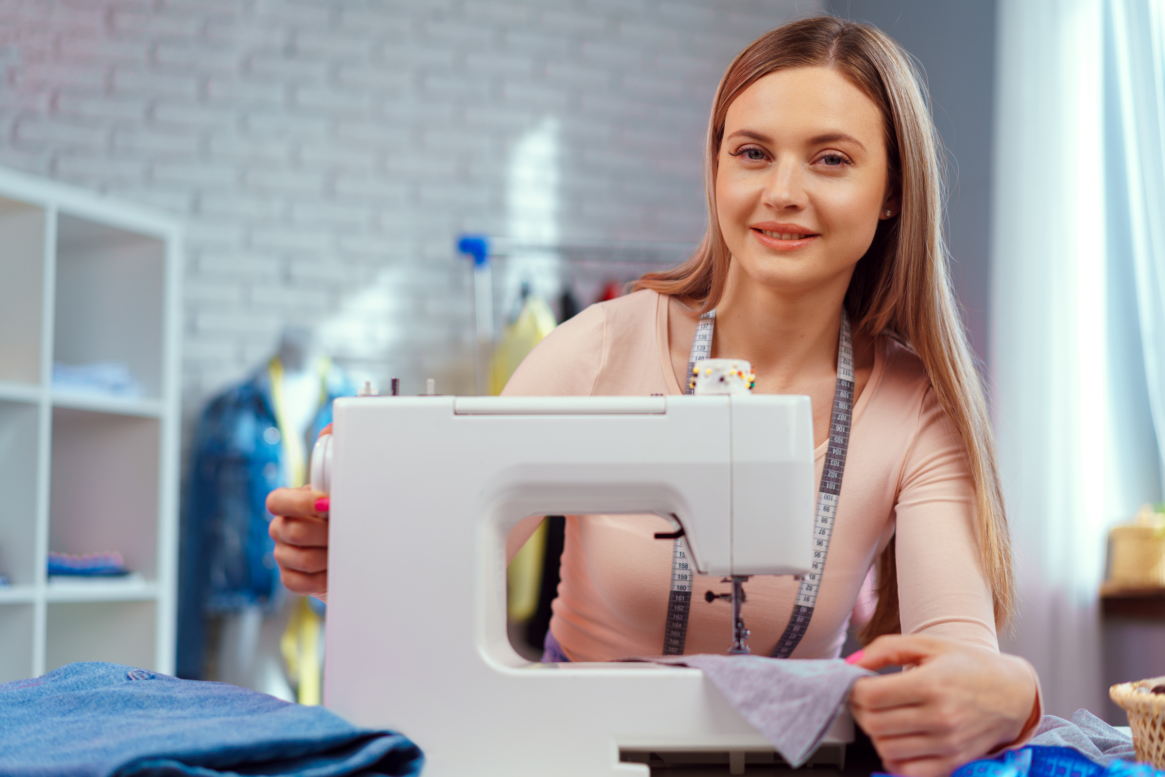 Cheerful young seamstress sitting at working table in her office